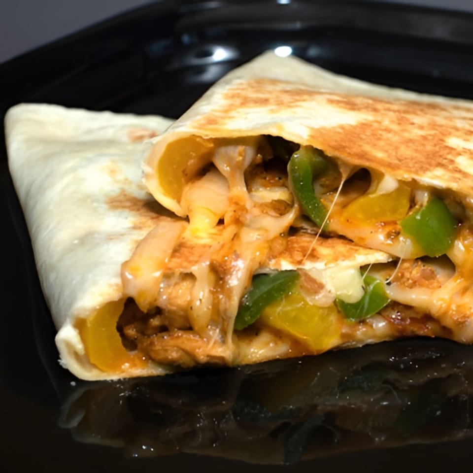 A cheesy quesadilla filled with chicken, green and yellow bell peppers, and onions on a black plate.