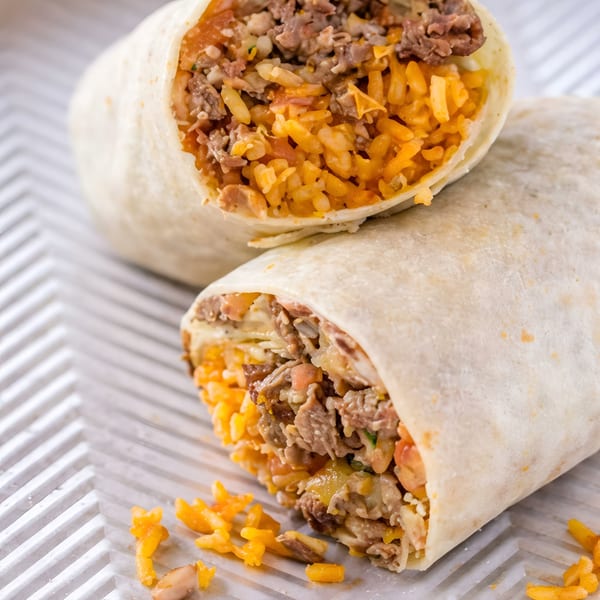 Two halves of a beef and rice burrito, with rice spilling out onto a white textured surface.