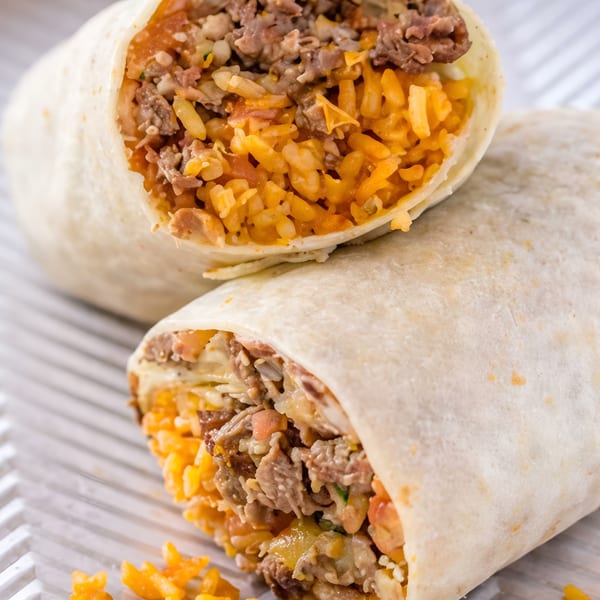 Two large burritos, one cut in half, revealing a filling of meat, orange rice, and cheese.