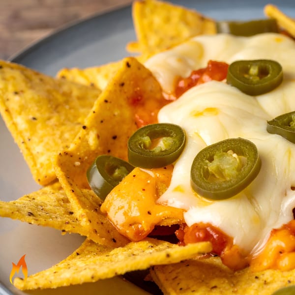 Close-up of cheesy nachos with melted white and orange cheese, salsa, and sliced jalapeños.
