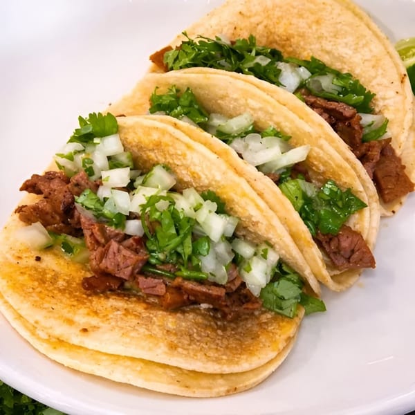 Three street tacos with meat, diced onions, and cilantro on a white plate.