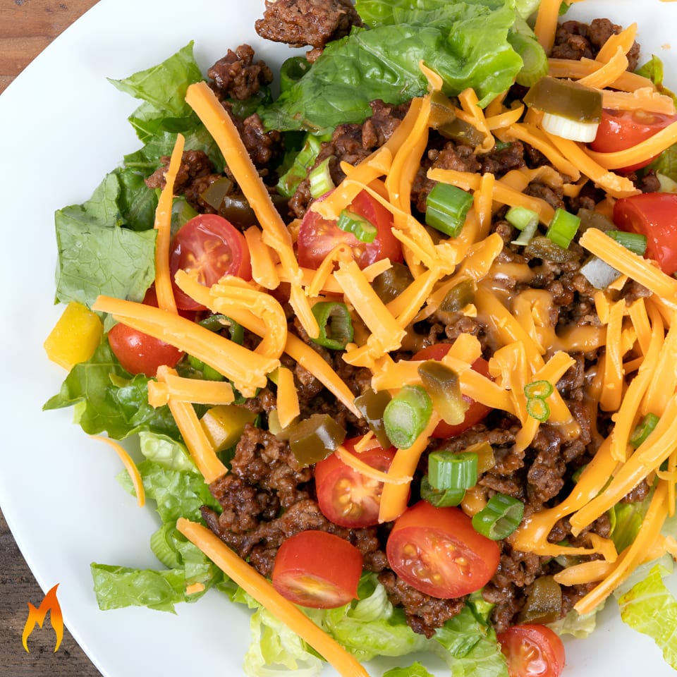 Taco salad with ground beef, shredded cheese, lettuce, tomatoes, green onions, and jalapeños.