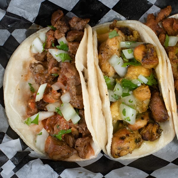 Two tacos, one with beef and one with chicken, topped with diced onions and cilantro.
